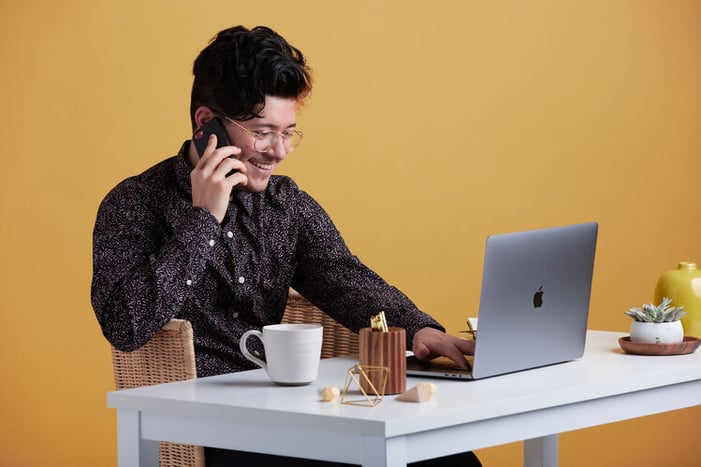 homme assis à un bureau souriant au téléphone devant son PC