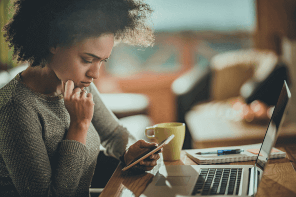 Frau schaut auf Handy am Arbeitsplatz und erstellt Gmail Spam-Filter