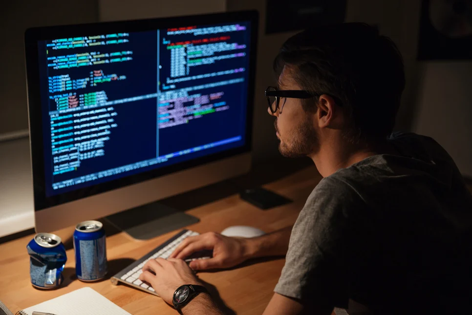 Nachdenklicher junger Programmierer am Computer abends zu Hause