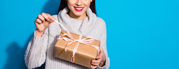 a woman in front of a blue background opens a present 