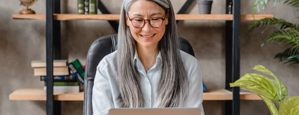 Woman smiles while sitting at her desk and typing on computer. 