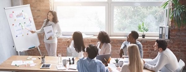 Business owner stands and points at a board with graphs on it during team meeting