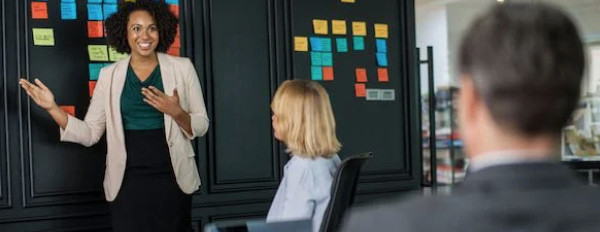 a female leader addresses her team in front of a wall with sticky notes on it