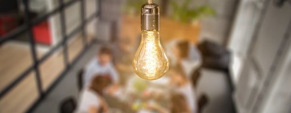 Image focuses on lit lightbulb with out of focus people in the background