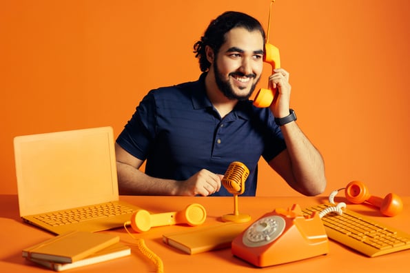 homem sentado em frente a uma mesa cor de laranja segura um telefone sem fio cor de laranja - foco em onboarding de cliente 