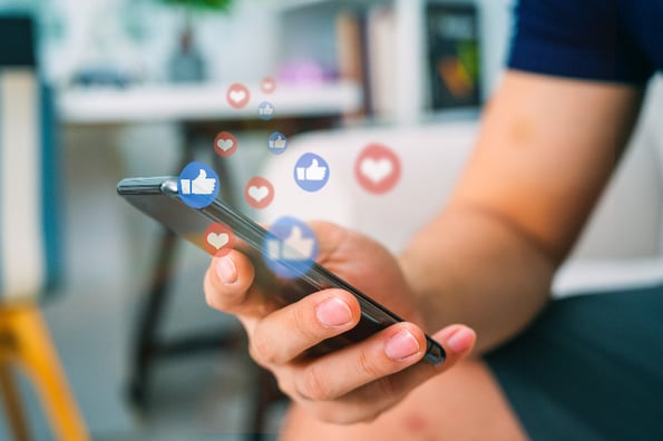 pessoa segura um aparelho de telefone celular e gráficos simulam likes em diferentes plataformas de rede social - aprenda a usar redes sociais no seu marketing digital 