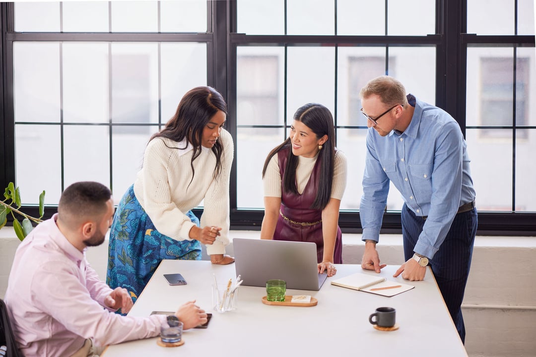 Three professionals standing around desk and one professional sitting down