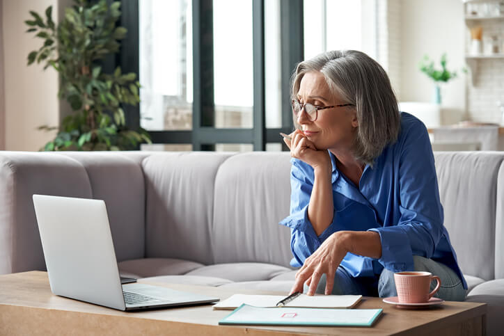 Frau mit Brille sitzt auf Sofa und schaut auf ihren Laptop