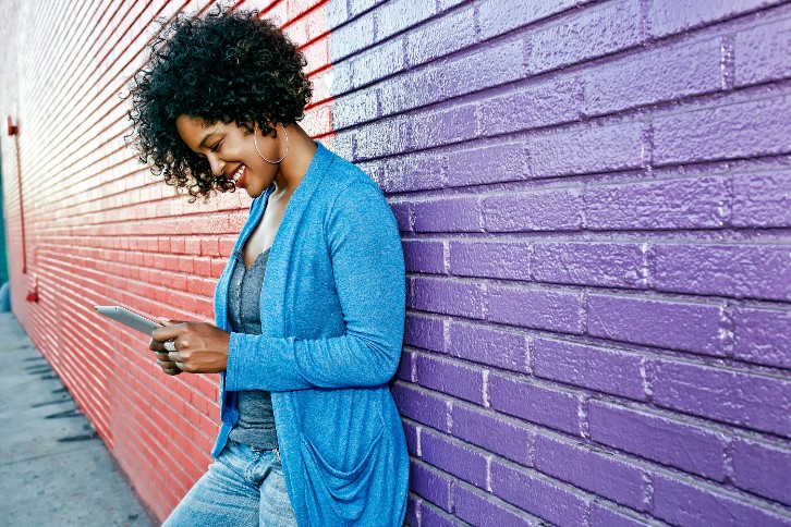 mulher encostada em parede lê conteúdo em aparelho de telefone móvel sobre os melhores horários para publicar no Instagram em 2023
